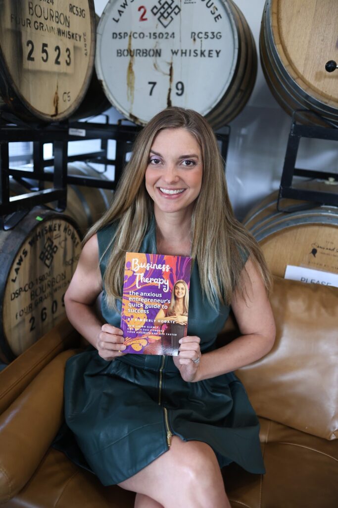Author Kimberly Hogate reading her book Business Therapy on a leather couch